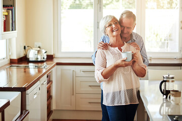 Hugging, coffee or old couple laughing in kitchen at home bonding or enjoying quality time together. Embrace, retirement or happy mature man talking, relaxing or drinking tea with funny senior woman - Powered by Adobe