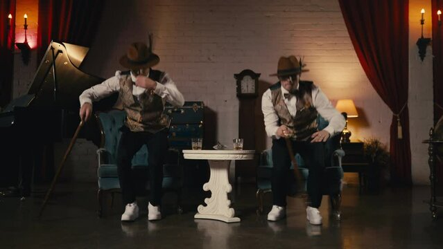Two guys in dandy style outfit synchronically dancing in retro theatre stage. Classy men dancers performing in jazz funk style, dancing with classic cane in hands. Music video, night show or event 4K