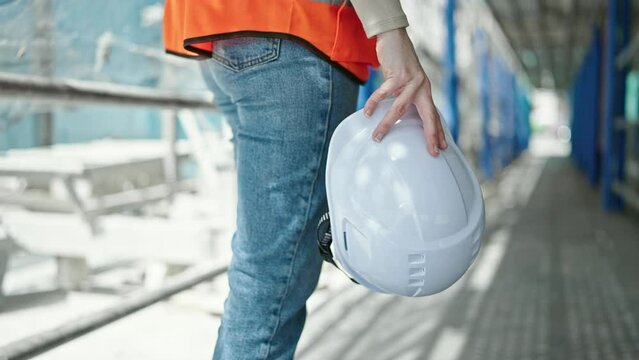 Young beautiful hispanic woman builder holding hardhat at street