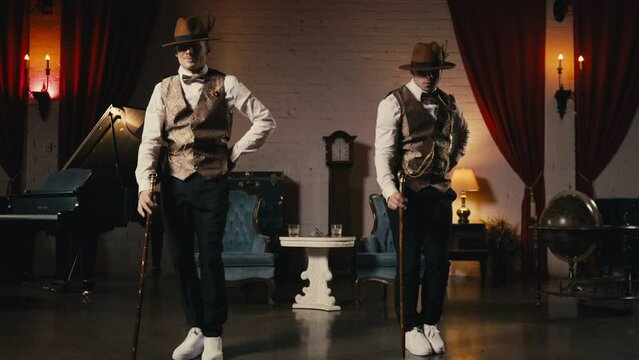 Classy male dancers performing in jazz funk style, dancing with classic cane in hands. Music video, night show or event 4K. Two guys in dandy style outfit synchronically dancing in retro theatre stage