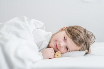 Happy little girl lying with toy bear on the bed at home