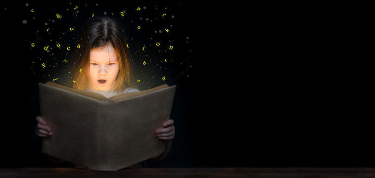 Surprised young girl reading magic book at night on dark background. Empty space for text