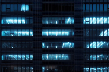 Fototapeta na wymiar Seamless skyscraper facade with blue tinted windows and blinds at night. Modern abstract office building background texture with glowing lights against dark black exterior walls. Generative AI