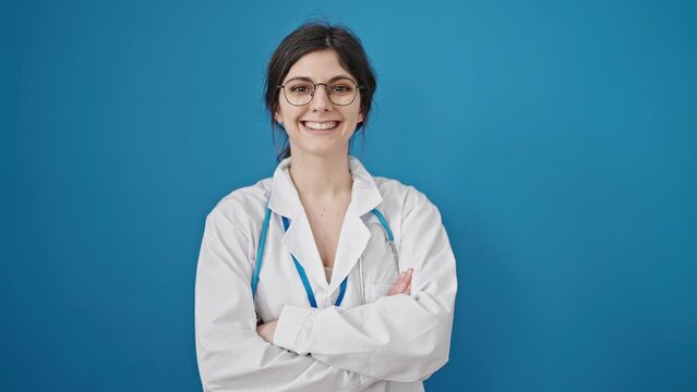 Young beautiful hispanic woman doctor smiling confident standing with arms crossed gesture over isolated blue background