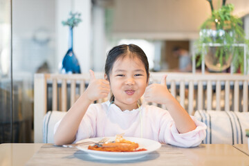 Asian child or kid girl enjoy eating breakfast by fried egg sausage bacon for morning food or...