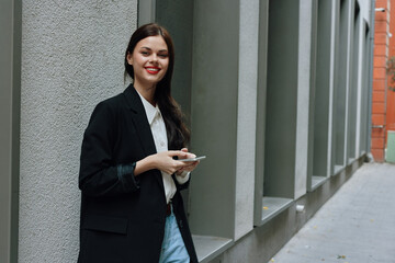 A woman smile with teeth with a phone in her hands walks around the city fashion on the street, spring travel, vacation in the city tourist freelancer, mobile communication and the Internet