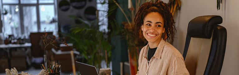 Smiling female florist working on laptop in floral studio and check customers order