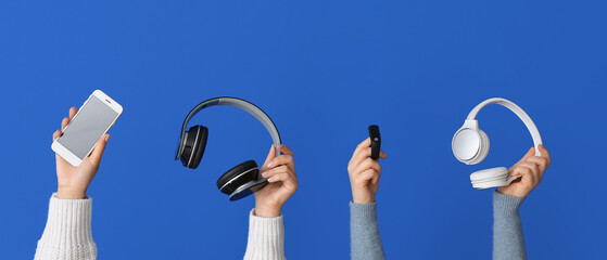 Female hands holding modern mobile phone, headphones and smart watch on blue background