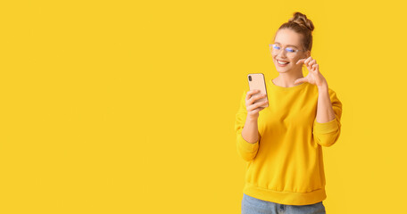 Young woman with mobile phone having online dating on yellow background with space for text