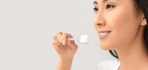 Beautiful Asian woman brushing teeth on light background with space for text
