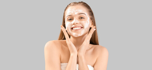 Beautiful young woman with soap foam on face against grey background