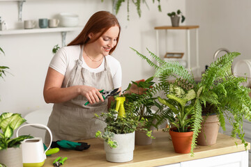 Young woman with pruner and green houseplants on table in kitchen