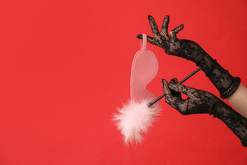 Woman with mask and feather stick from sex shop on red background