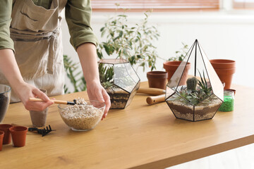 Female gardener making florarium on table at home, closeup