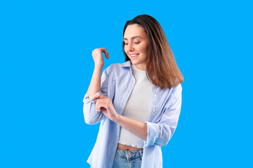 Beautiful young woman rolling up her sleeve on light blue background