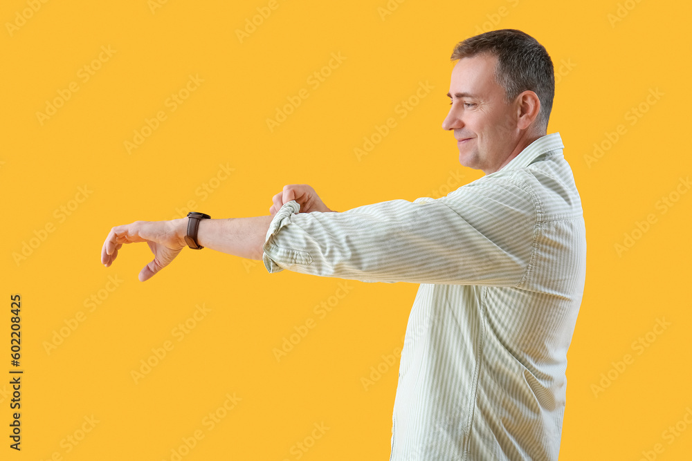 Wall mural Mature man rolling up his sleeve on yellow background - Wall murals