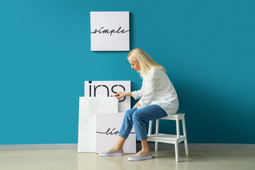 Mature woman hanging posters on blue wall