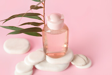 Obraz na płótnie Canvas Bottle of micellar water with plant branch and spa stones on pink background