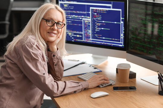 Mature female programmer working with computer at table in office