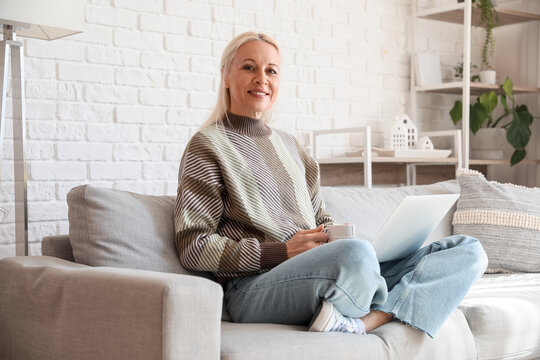 Mature female programmer with cup of coffee and laptop working at home