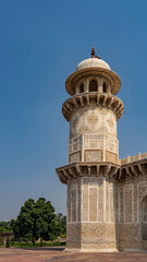 Fototapeta na wymiar Details of the architecture of the ancient tomb of Itmad-Ud-Daulah. Marble minaret with balconies and a dome against the blue sky. On the walls there are ornaments, inlays of precious stones. India.