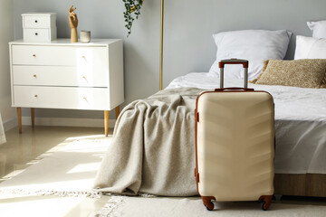 Fototapeta Big suitcase near bed in light room obraz