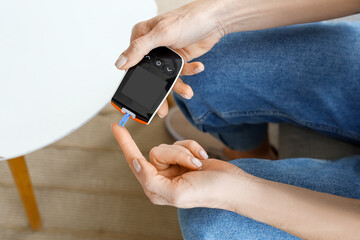 Mature diabetic woman measuring blood sugar level with glucometer at home, closeup