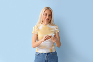 Mature diabetic woman measuring blood sugar level with glucometer on blue background