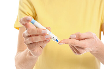 Mature diabetic woman using lancet pen on white background, closeup
