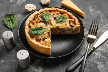 Mushroom pie with spinach leaves and cutlery on black grunge table