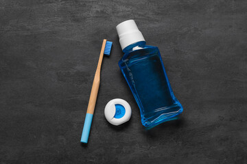 Dental floss with blue bamboo toothbrush and mouthwash on black grunge background