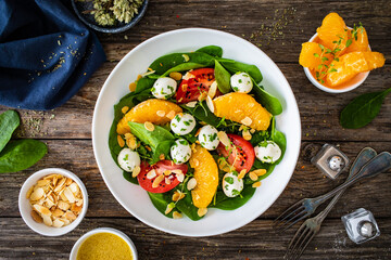 Mozzarella salad with leafy greens, orange and tomatoes  on wooden table
