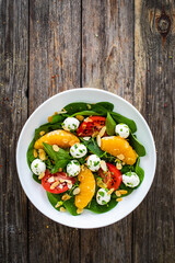 Mozzarella salad with leafy greens, orange and tomatoes  on wooden table
