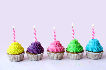 Tasty cupcakes with birthday candles on lilac background