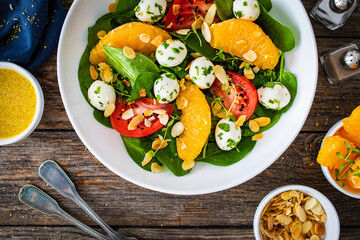 Mozzarella salad with leafy greens, orange and tomatoes  on wooden table
