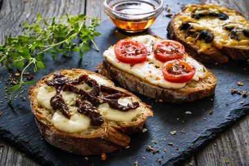 Tasty sandwiches - baked bread with cheese, olives, sun dried tomatoes, mushrooms and thyme on wooden table
