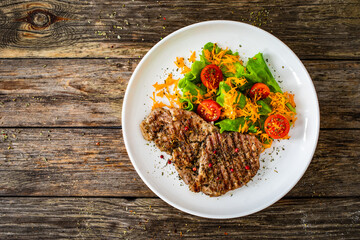 Grilled pork steaks with fresh vegetable salad on wooden table 