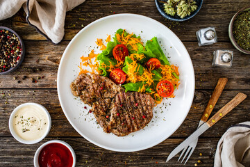 Grilled pork steaks with fresh vegetable salad on wooden table 