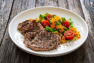 Grilled pork steaks with fresh vegetable salad on wooden table 