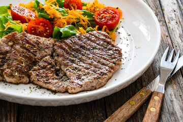 Grilled pork steaks with fresh vegetable salad on wooden table 