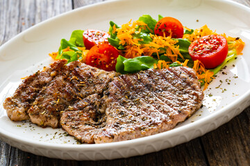 Grilled pork steaks with fresh vegetable salad on wooden table 