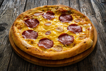 Circle pepperoni pizza with mozzarella cheese and onion on wooden table 