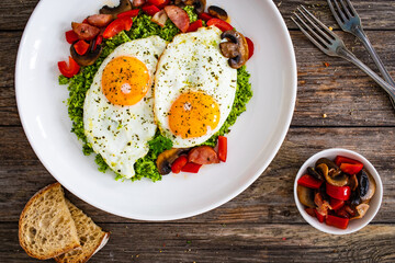 Breakfast - sunny side up eggs, grated broccoli, stir fried vegetables and sliced sausages served on wooden table
