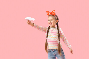 Little girl with paper plane on pink background. Children's Day celebration