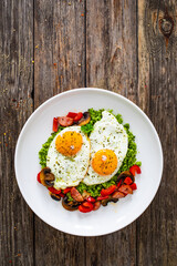 Breakfast - sunny side up eggs, grated broccoli, stir fried vegetables and sliced sausages served on wooden table
