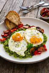 Breakfast - sunny side up eggs, grated broccoli, stir fried vegetables and sliced sausages served on wooden table
