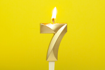 Burning gold birthday candle on yellow background. Number 7.