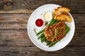 Barbecued pork neck and asparagus on wooden table
