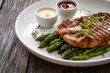 Barbecued pork neck and asparagus on wooden table
