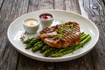 Barbecued pork neck and asparagus on wooden table